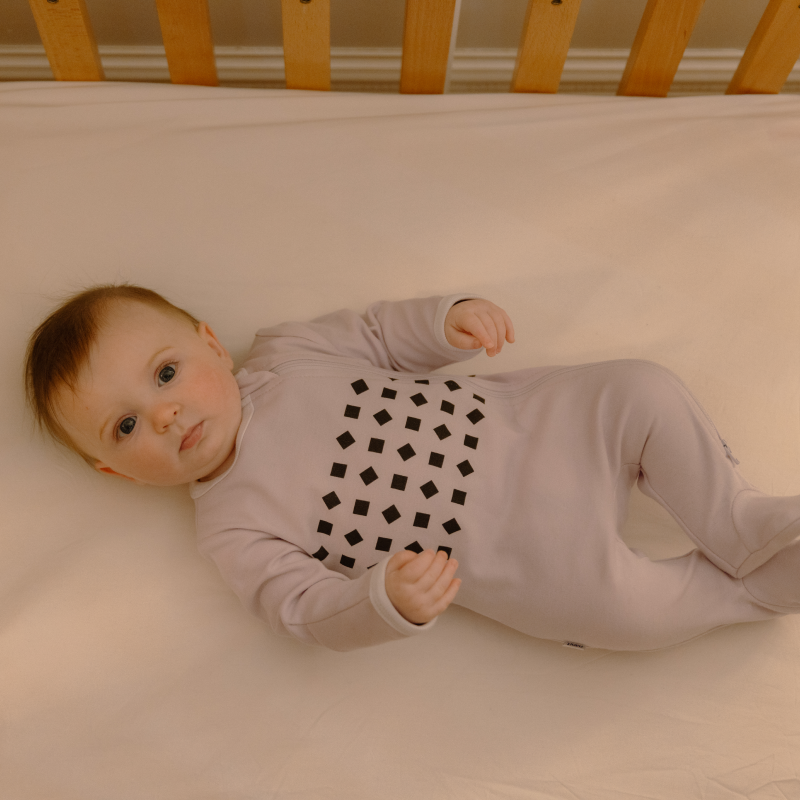 baby laying in crib in lilac pajamas #color_lilac