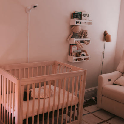 baby sleeping in crib while nanit pro camera + wall mount is on wall in room 