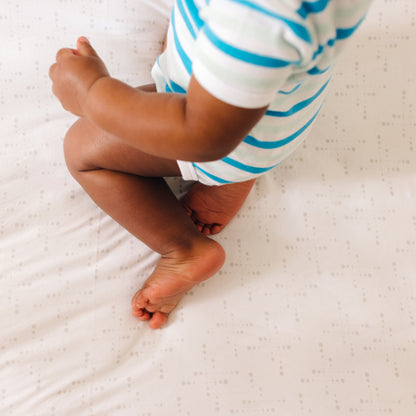 Baby sitting on Nanit Knit Crib Sheet in pink sunburst