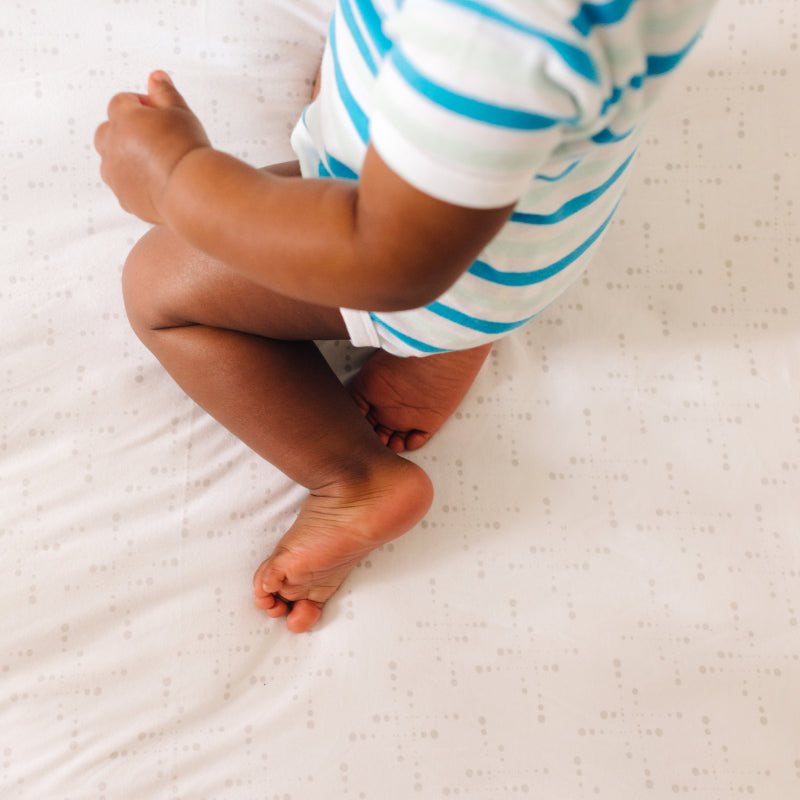 Baby sitting on Nanit Knit Crib Sheet in pink sunburst